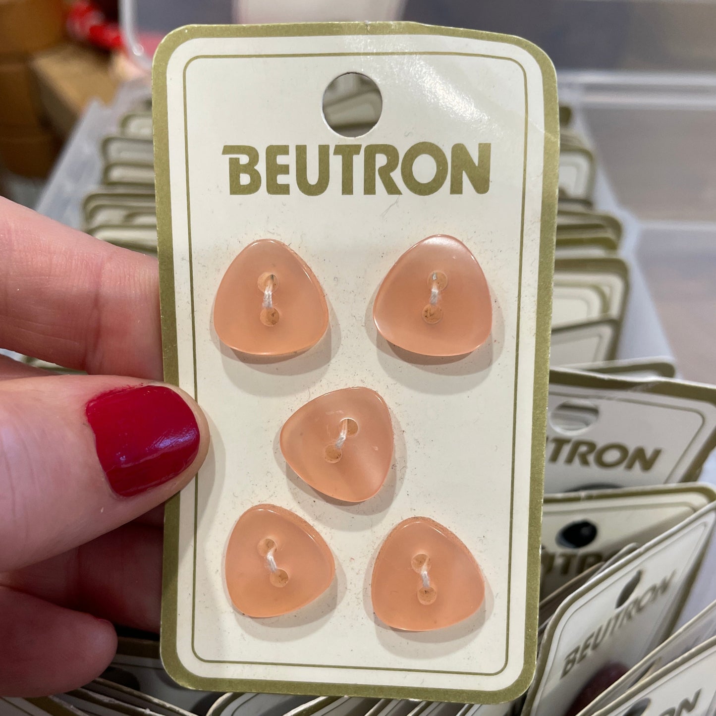 Pack of Beutron buttons held by a hand with red nail polish.