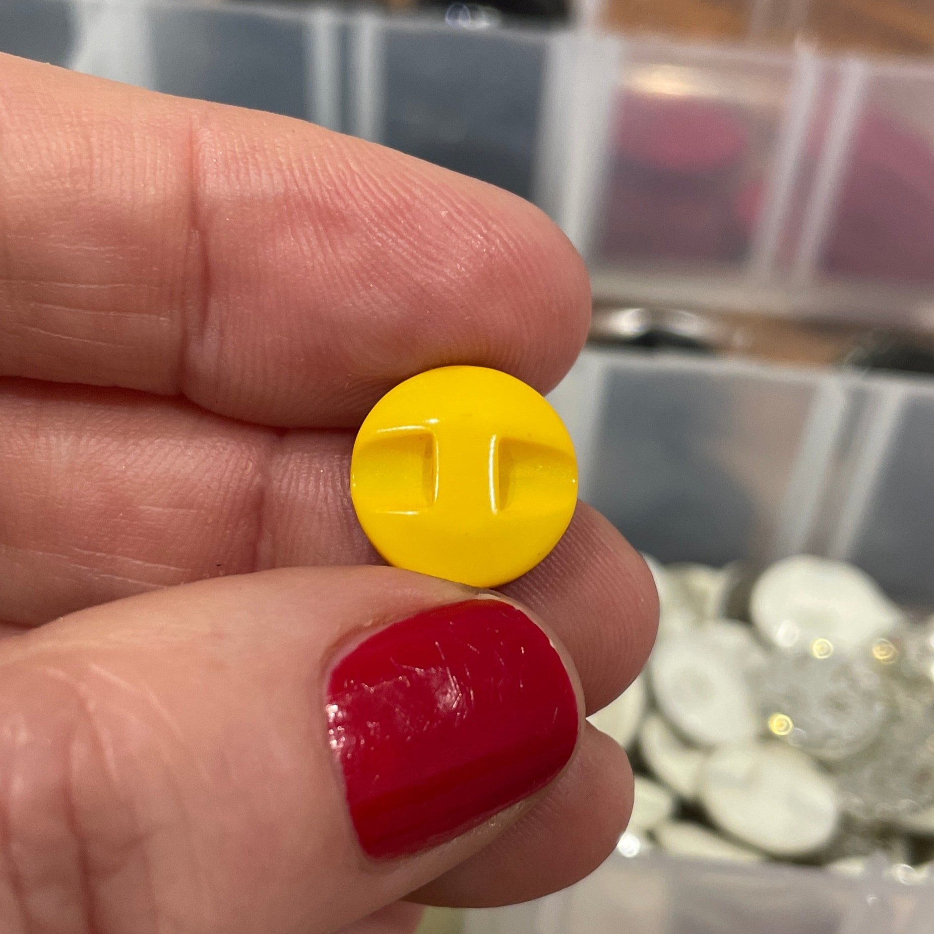 Hand holding a yellow button with a blurred background of button containers.