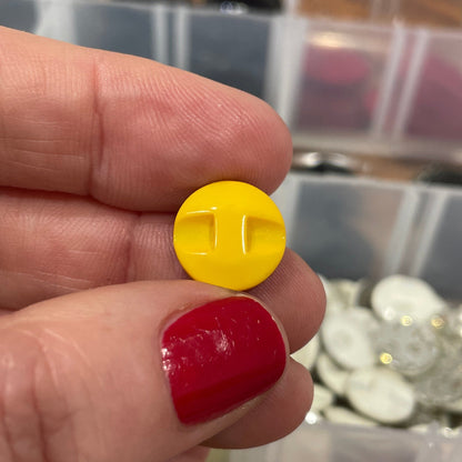 Hand holding a yellow button with a blurred background of button containers.