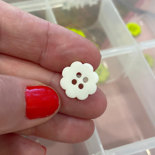 Hand holding a white flower-shaped button with a clear container of buttons in the background