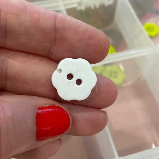 White button held between fingers with a clear container of buttons in the background