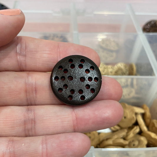 Hand holding a black button with holes against a background of various buttons.