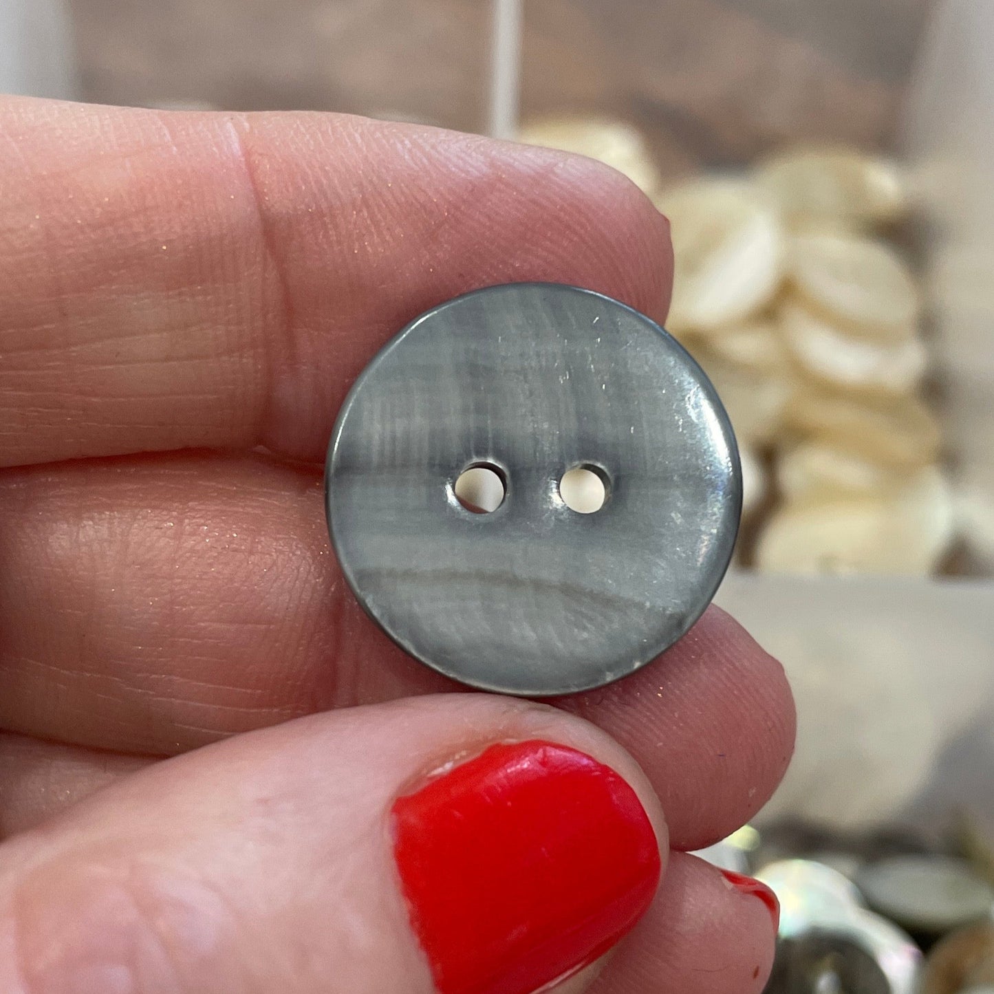 Hand holding a silver button with a blurred background of button collection