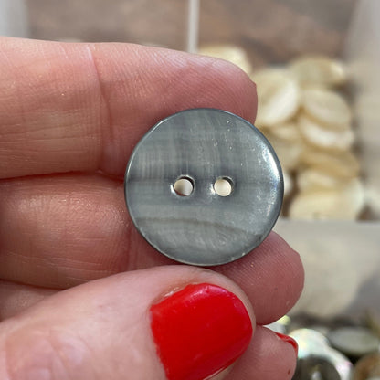 Hand holding a silver button with a blurred background of button collection