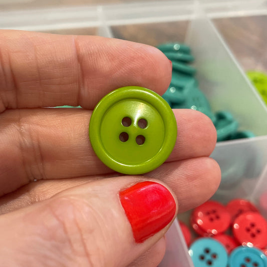 Hand holding a green button with a container of colorful buttons in the background