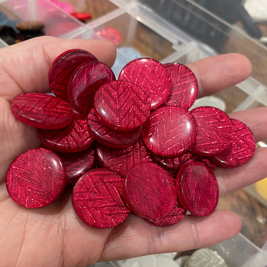 Hand holding red textured buttons with a container of various colored buttons in the background.