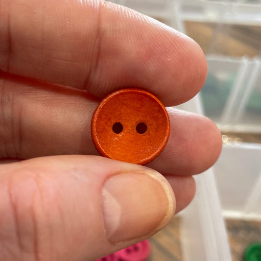 Hand holding an orange button with a blurred background of button assortment
