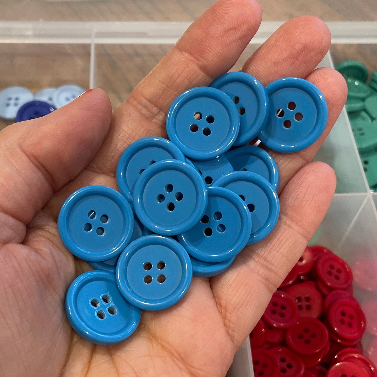 Hand holding blue buttons with a container of colorful buttons in the background