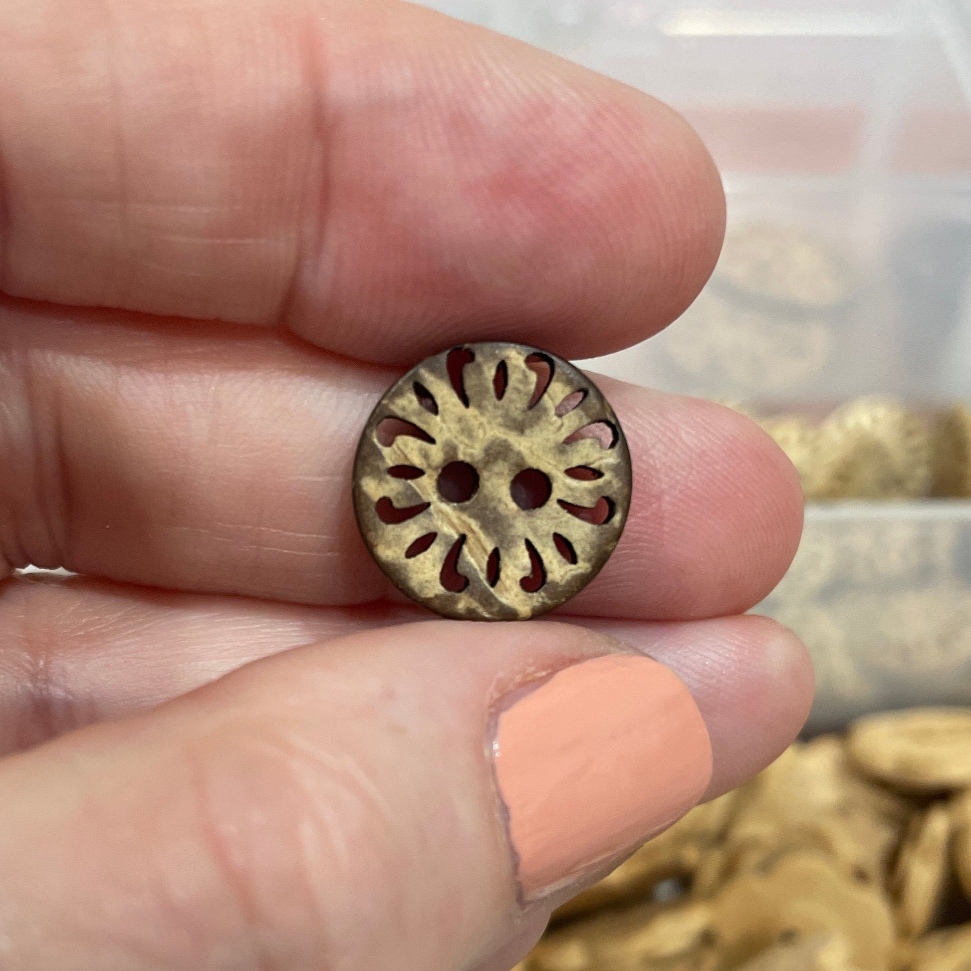 Hand holding a gold button with a container of buttons in the background