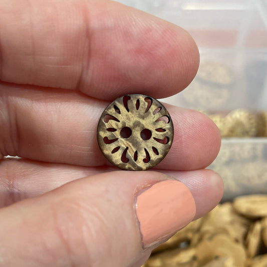 Hand holding a gold button with a container of buttons in the background