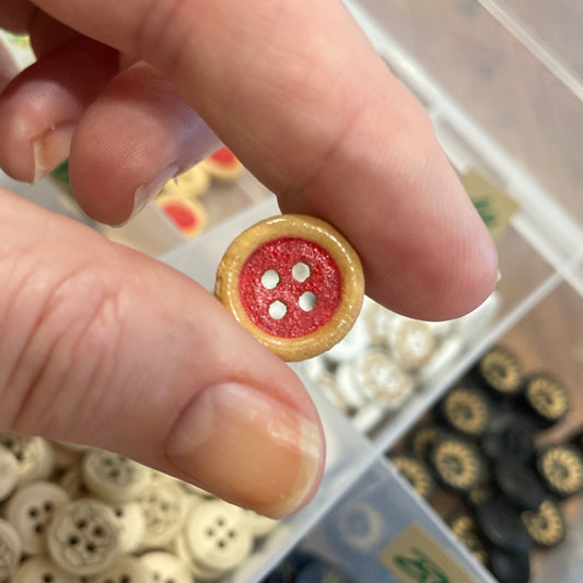 Hand holding a red button with a collection of buttons in the background