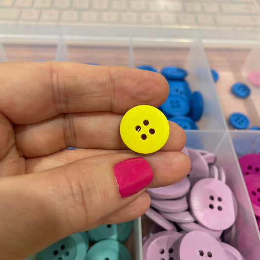 Hand holding a yellow button with a container of assorted buttons in the background