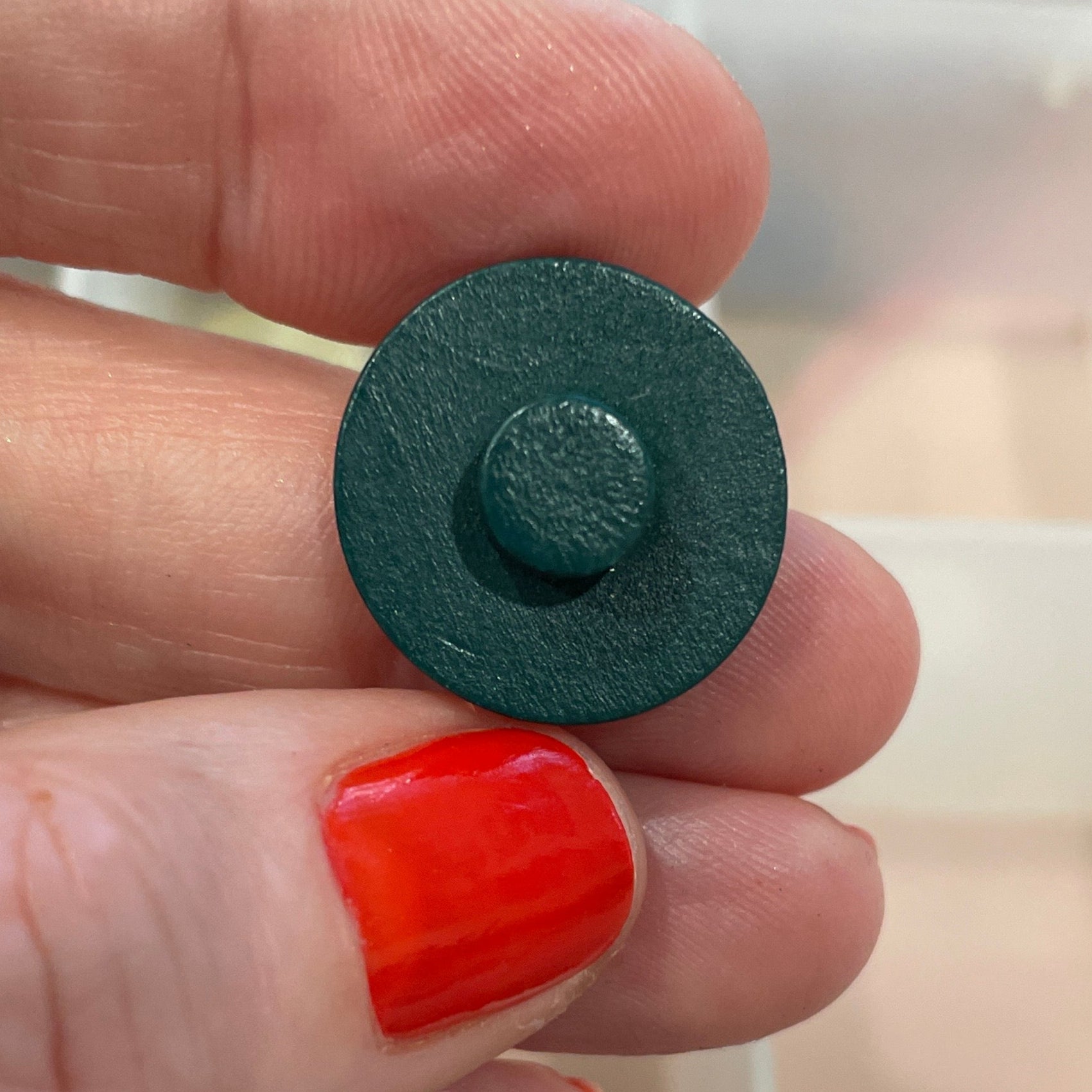 Person holding a black button with a clear container of buttons in the background