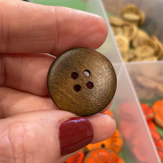 Hand holding a brown button with a container of colorful buttons in the background