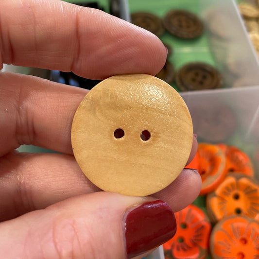 Hand holding a yellow button with a container of colorful buttons in the background