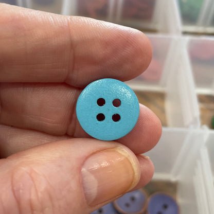 Hand holding a blue button with a blurred background of button containers.