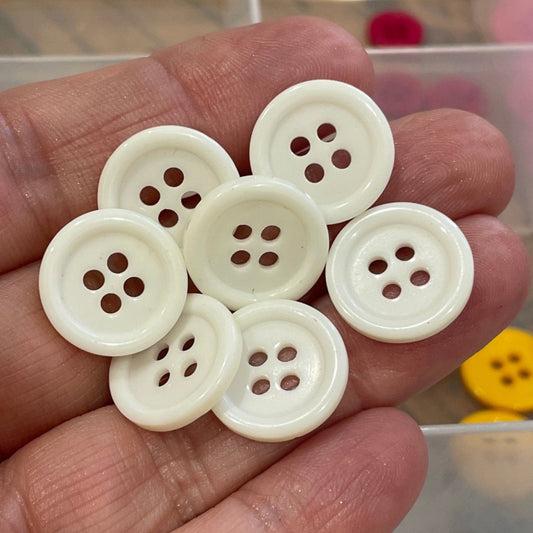 Hand holding white buttons with a clear container of colorful buttons in the background