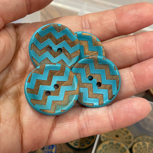 Hand holding decorative buttons with a clear container of more buttons in the background