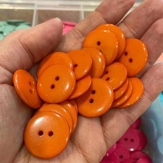 Hand holding orange buttons with a blurred background of more buttons.