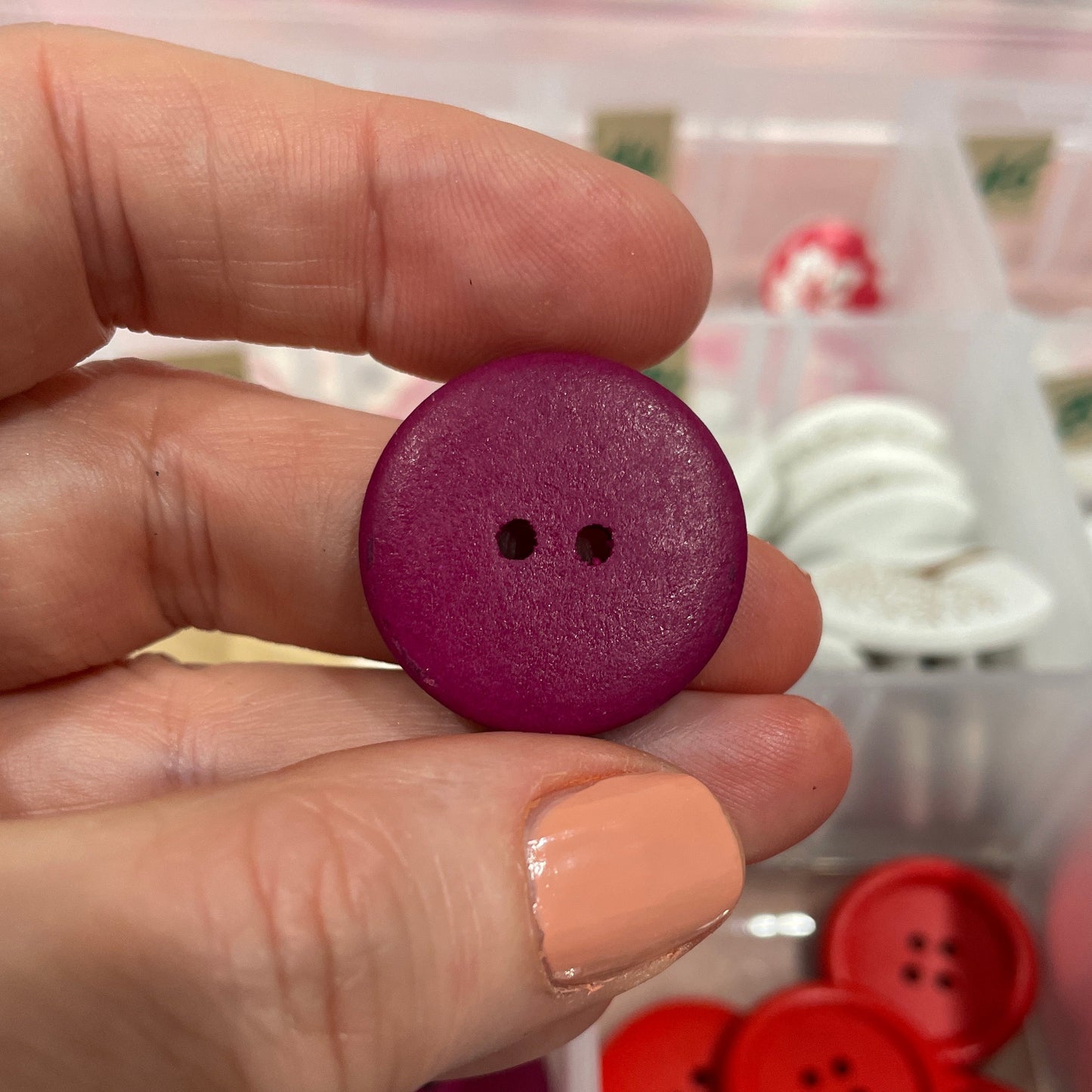 Hand holding a purple button with a blurred background of various buttons