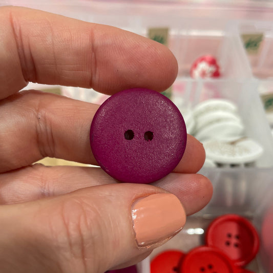 Hand holding a purple button with a blurred background of various buttons