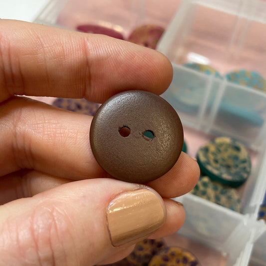 Person holding a brown button with a container of buttons in the background