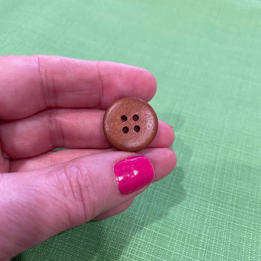 Brown button held between fingers against a green fabric background