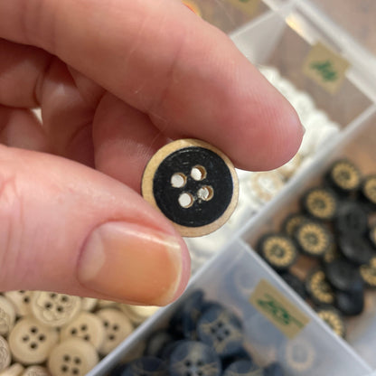 Hand holding a black button with a blurred background of button collection