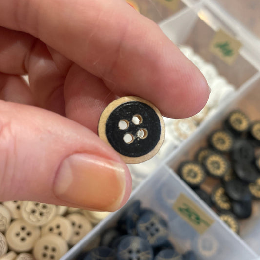 Hand holding a black button with a blurred background of button collection