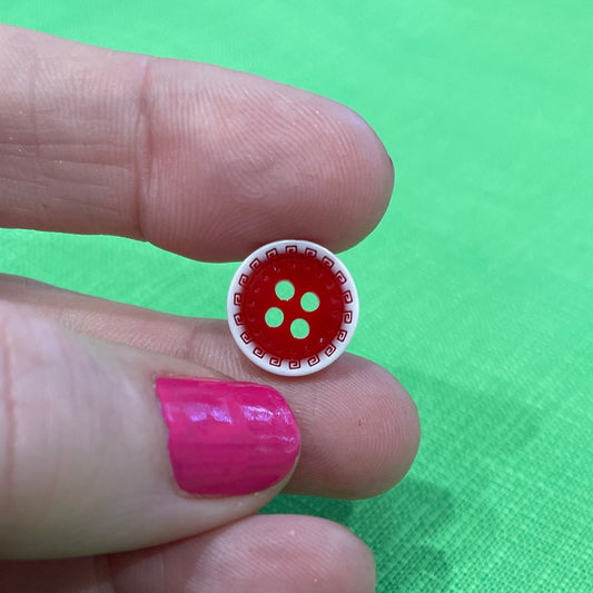 Small red button with white border held between fingers against a green fabric background