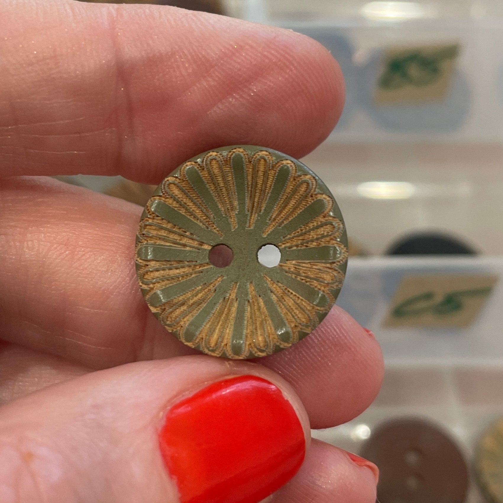Hand holding a decorative button with a background of button collection