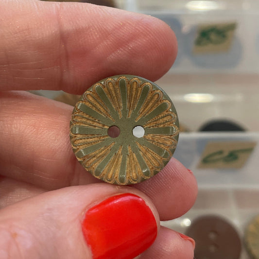 Hand holding a decorative button with a background of button collection