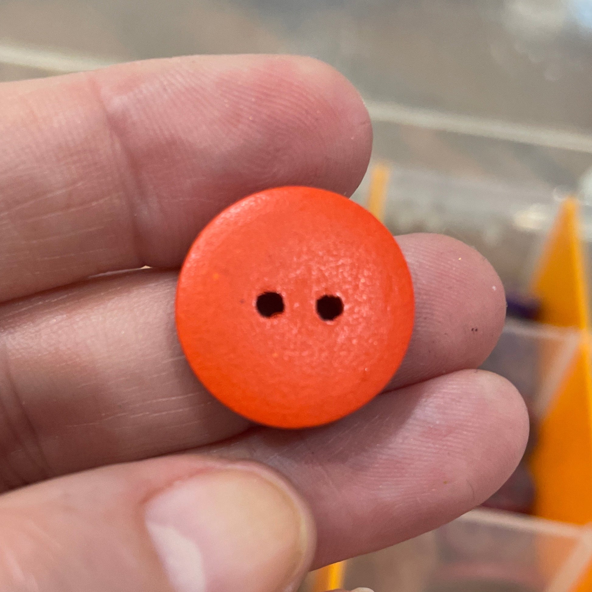 Orange button held between fingers with a container of buttons in the background