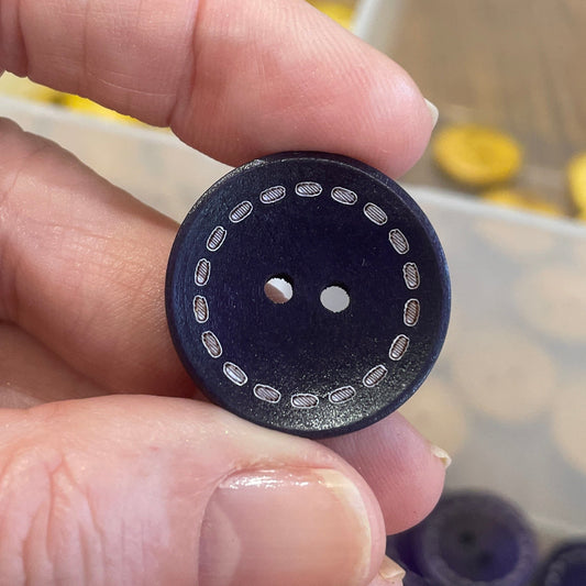 Hand holding a black button with white dots against a background of various buttons in a container.