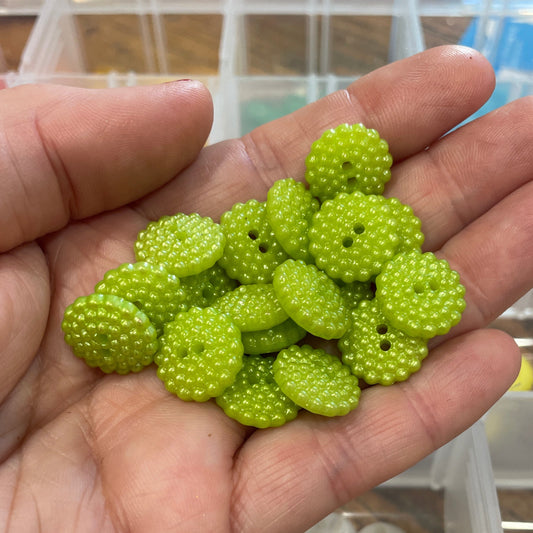 Hand holding green buttons with a container of buttons in the background