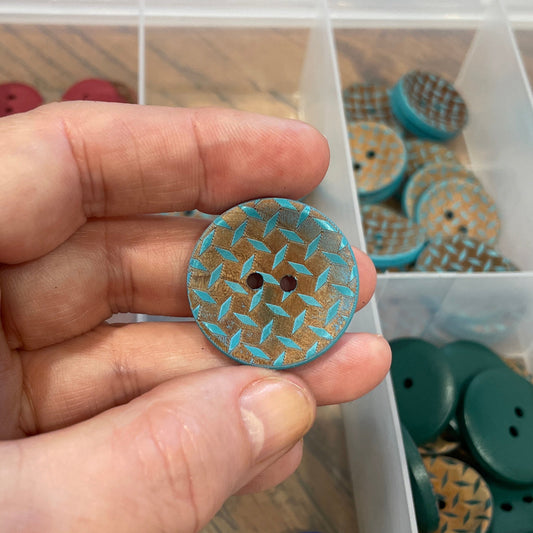 Hand holding a button with a clear container of assorted buttons in the background