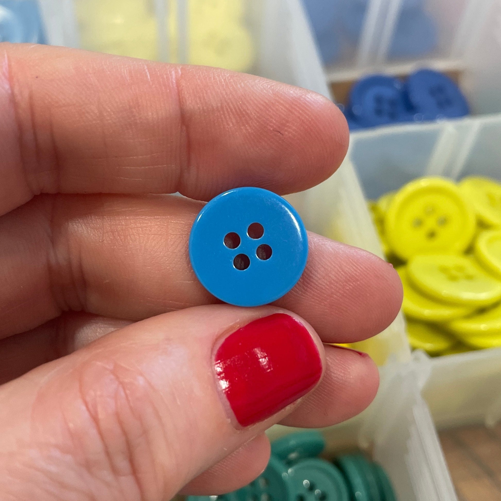 Hand holding a blue button with a blurred background of button containers.