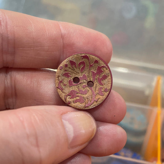 Hand holding two floral-patterned buttons with a container of buttons in the background.