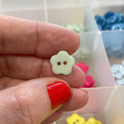 Hand holding a small white flower-shaped button with a background of colorful buttons in a box.