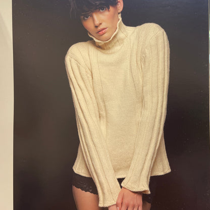 Person wearing a cream sweater with a dark background