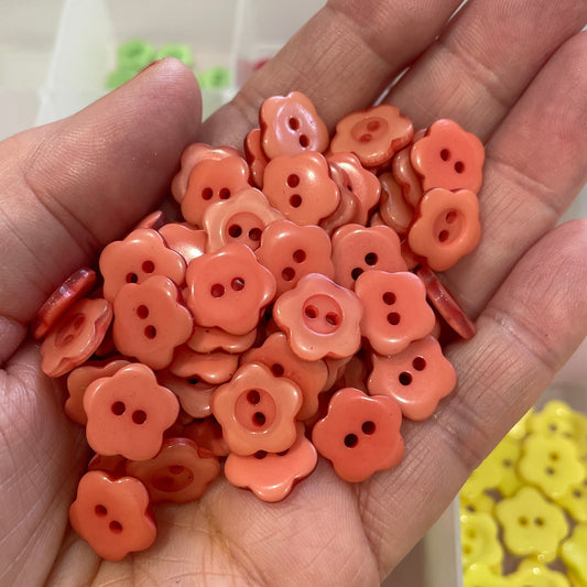 Hand holding a small pile of coral-colored flower-shaped buttons with a blurred background.