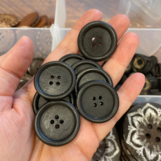 Hand holding black buttons with a clear container of buttons in the background