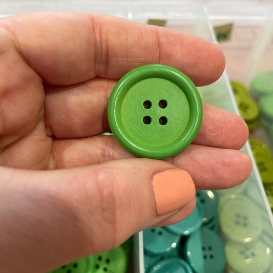 Green button held in a hand with a container of buttons in the background