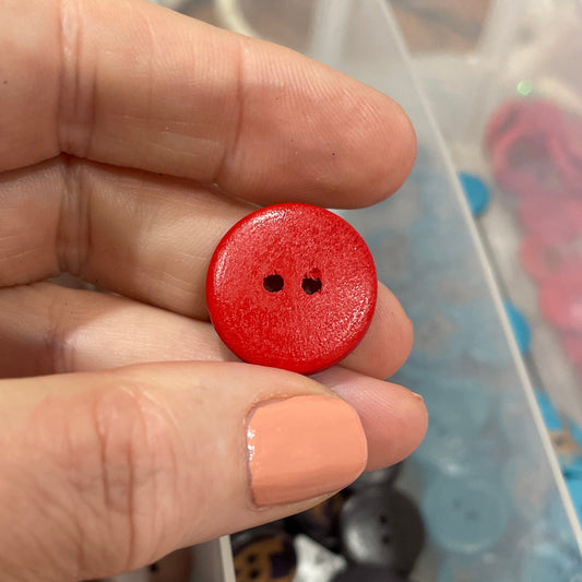 Red button held between fingers with a container of buttons in the background