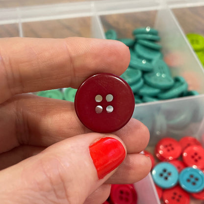 Hand holding a red button with colorful buttons in containers in the background