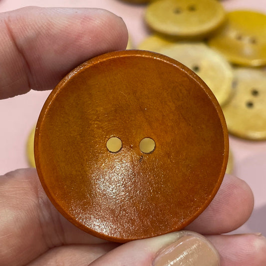 Hand holding a brown button with two holes, surrounded by colorful buttons on a pink surface.