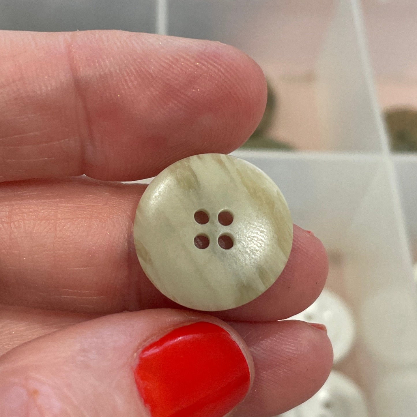 Hand holding a button with a clear container of buttons in the background