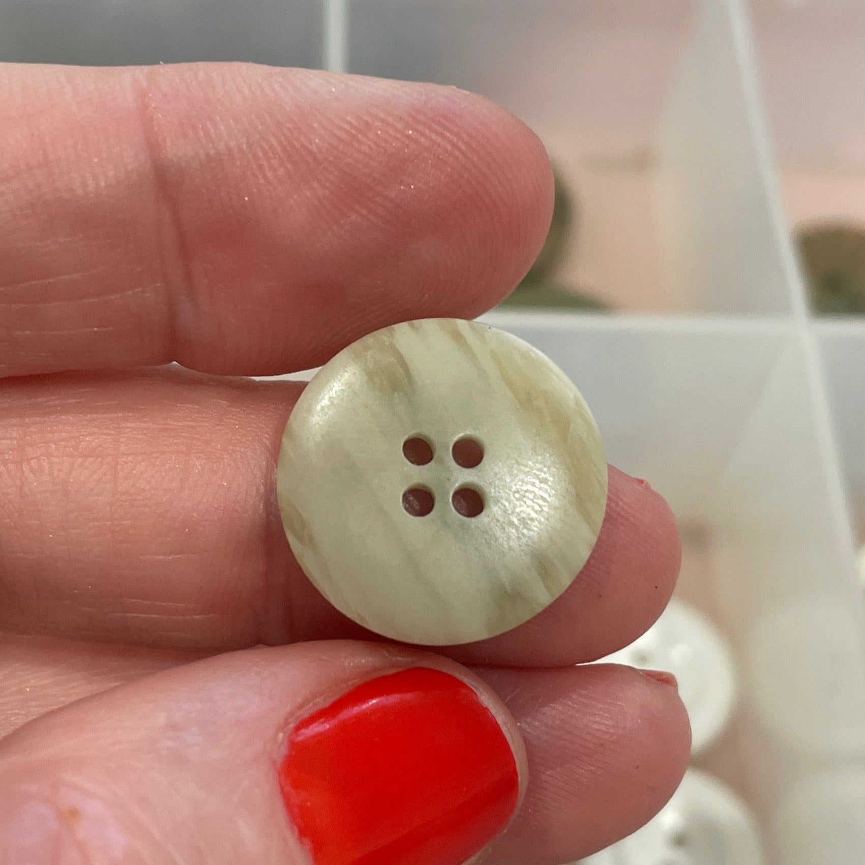 Hand holding a button with a clear container of buttons in the background