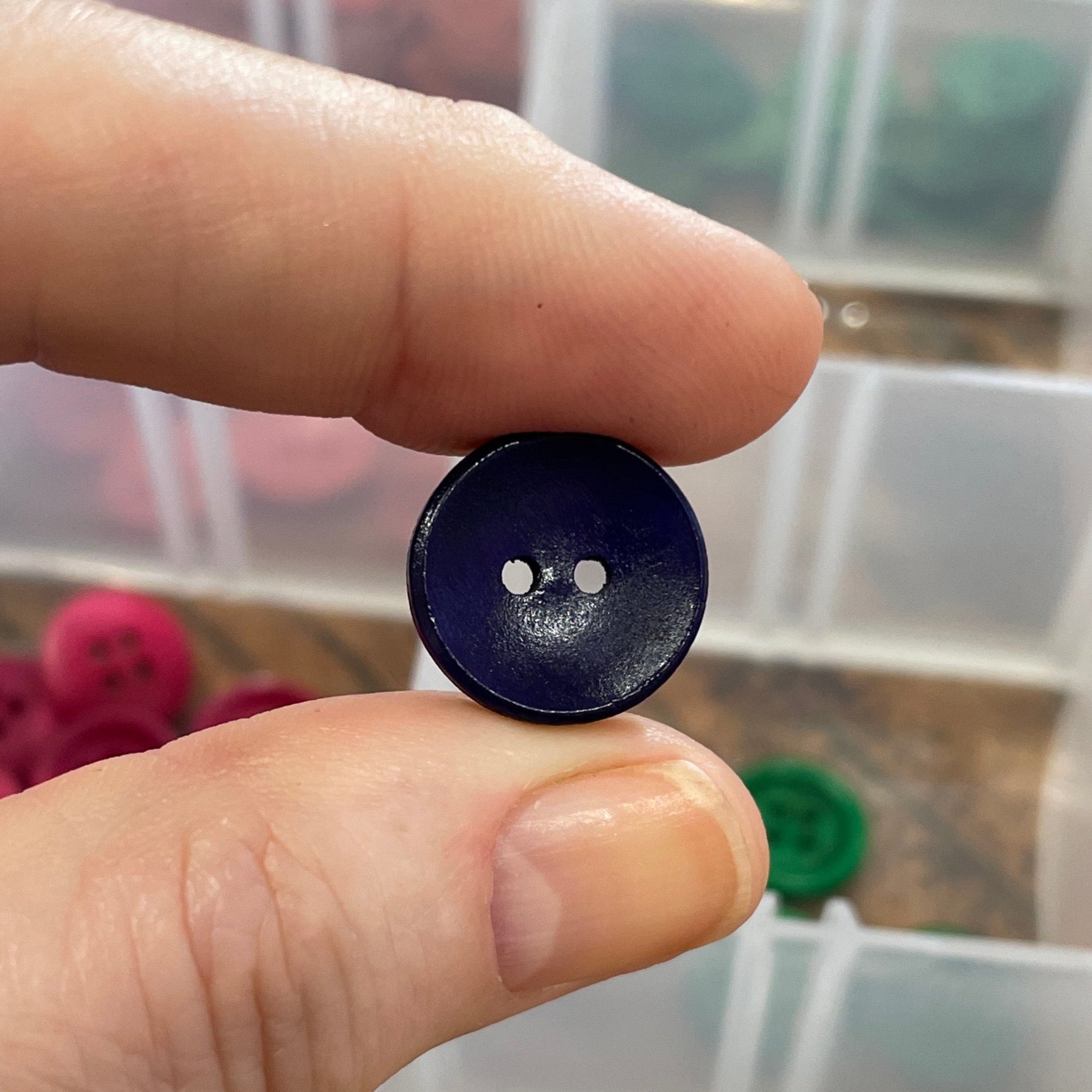 Hand holding a purple button with a clear container of buttons in the background