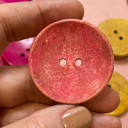 Hand holding a pink button with other buttons in the background